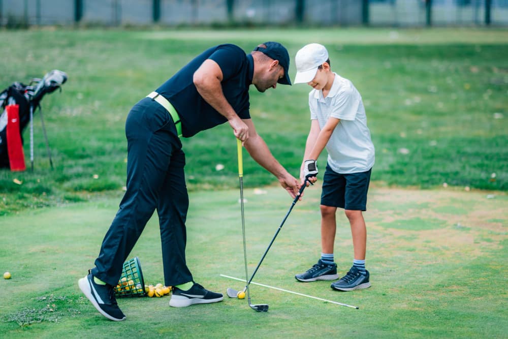 PGA coach guiding a young golfer's swing at the driving range during a Westfield Golf Academy lesson